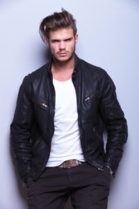 serious man in leather jacket standing against gray wall
